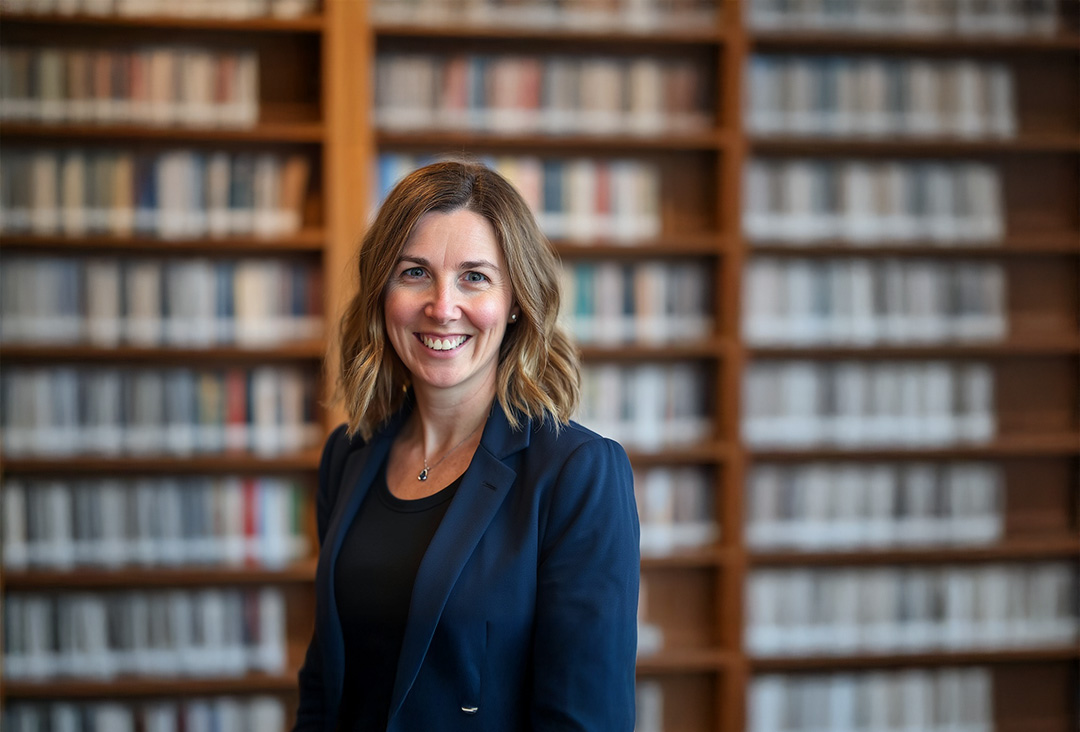 Kim Coshaw of Child Expert Network standing in front of bookshelves wearing a navy jacket